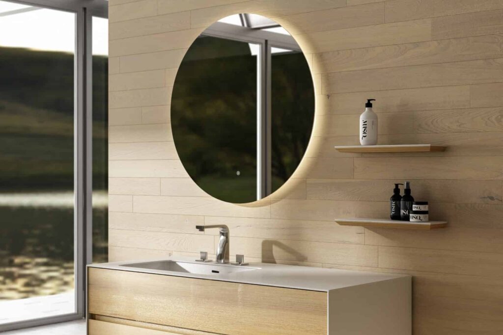 Salle de bain épurée dans un décor de bois clair avec vanité suspendue, miroir DEL rond à bouton tactile et 2 tablette.