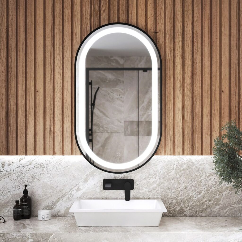 Miroir ovale DEL de la collection Effect par Kalia, au-dessus d'une vasque blanche et d'un robinet mural noir.