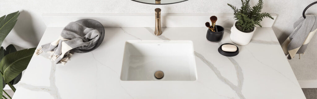 Vanité de salle de bain dotée d'un comptoir de quartz aux teintes douces et naturelles, avec robinet doré, accessoires et verdure